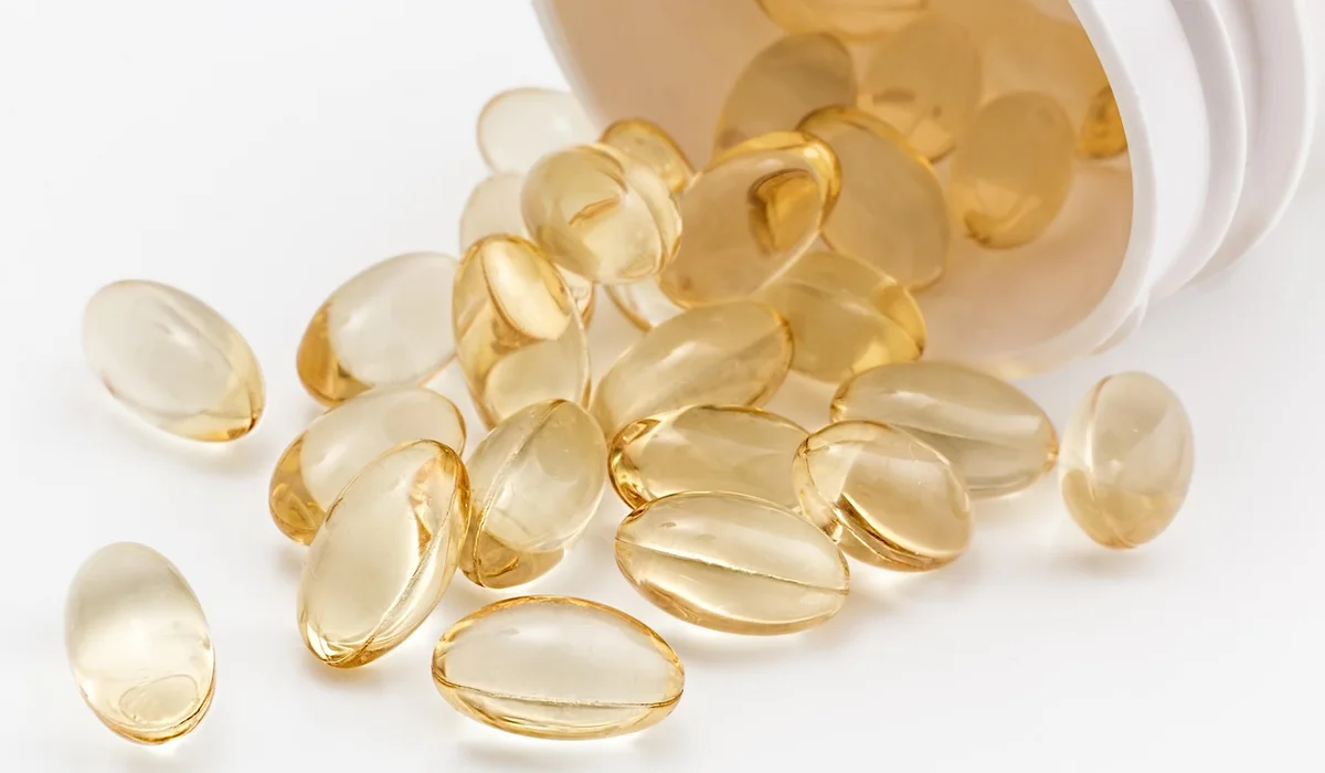 Assorted soft gel capsules spilling from a white bottle onto a white surface