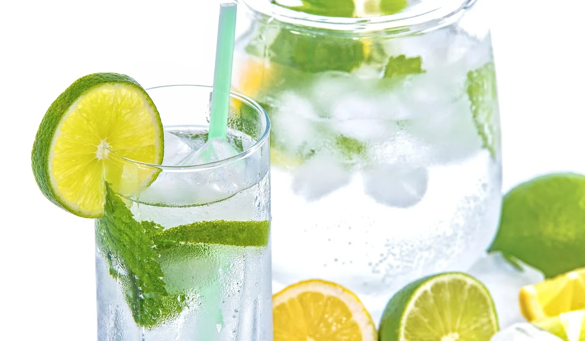 Glass of lime water with a pitcher and sliced lemons and limes in the background