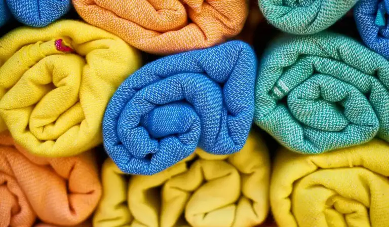 Vibrant rolled towels in blue, yellow, orange, and green stacked together.