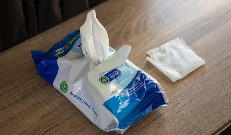 Opened pack of disinfectant wipes on a wooden table with a tissue nearby.