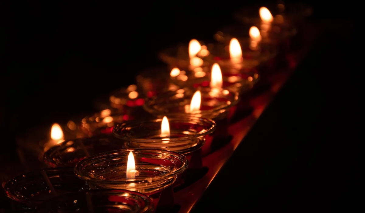 Row of lit tealight candles in glass holders glowing in a dark room