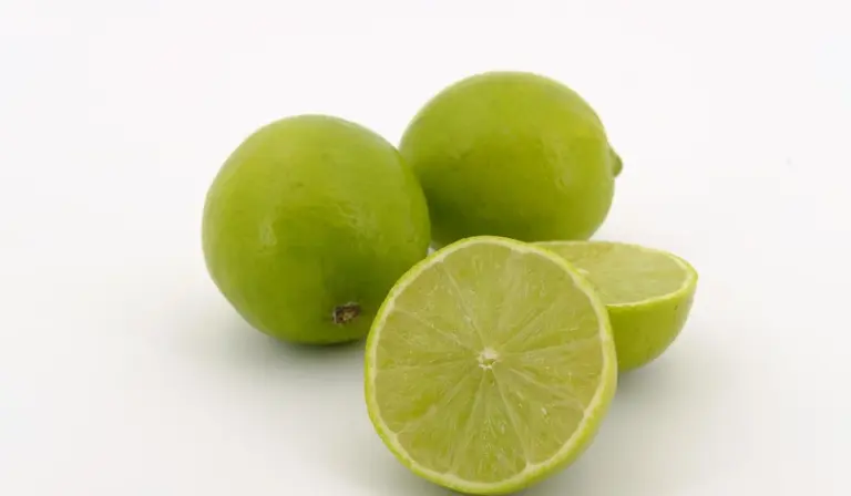 Three green limes on a white background, one cut open to reveal the juicy interior