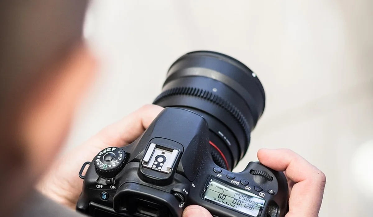 Close-up of a photographer holding a DSLR camera with a large lens
