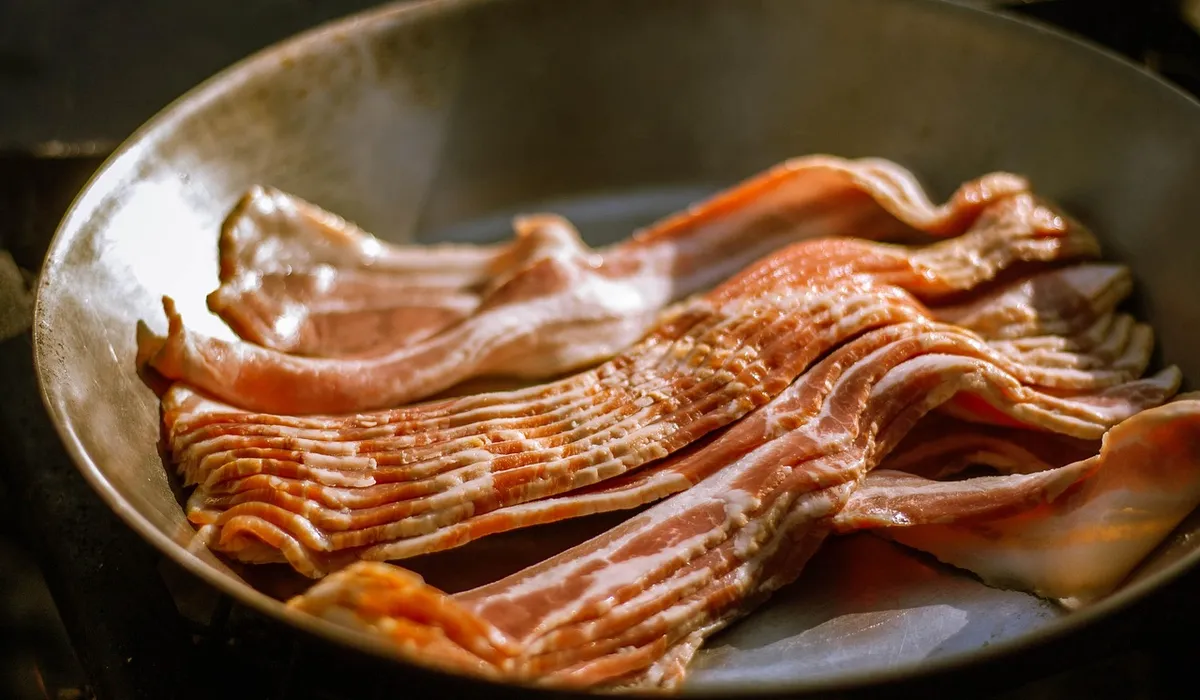 Raw slices of bacon in a metal skillet.