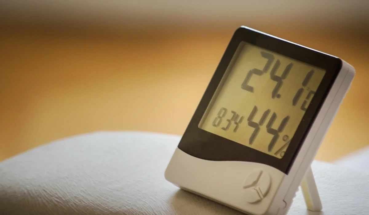 Close-up of a digital thermometer displaying temperature and humidity for a parrot's habitat.