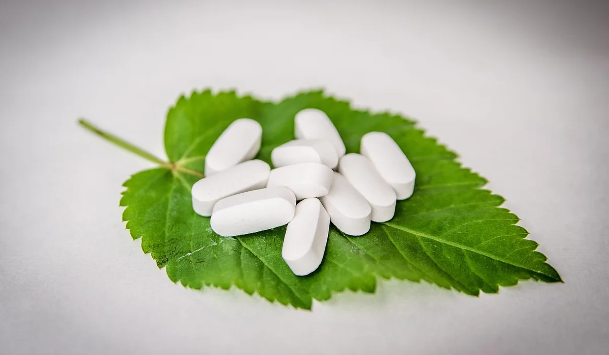 White oblong pills arranged on a bright green leaf