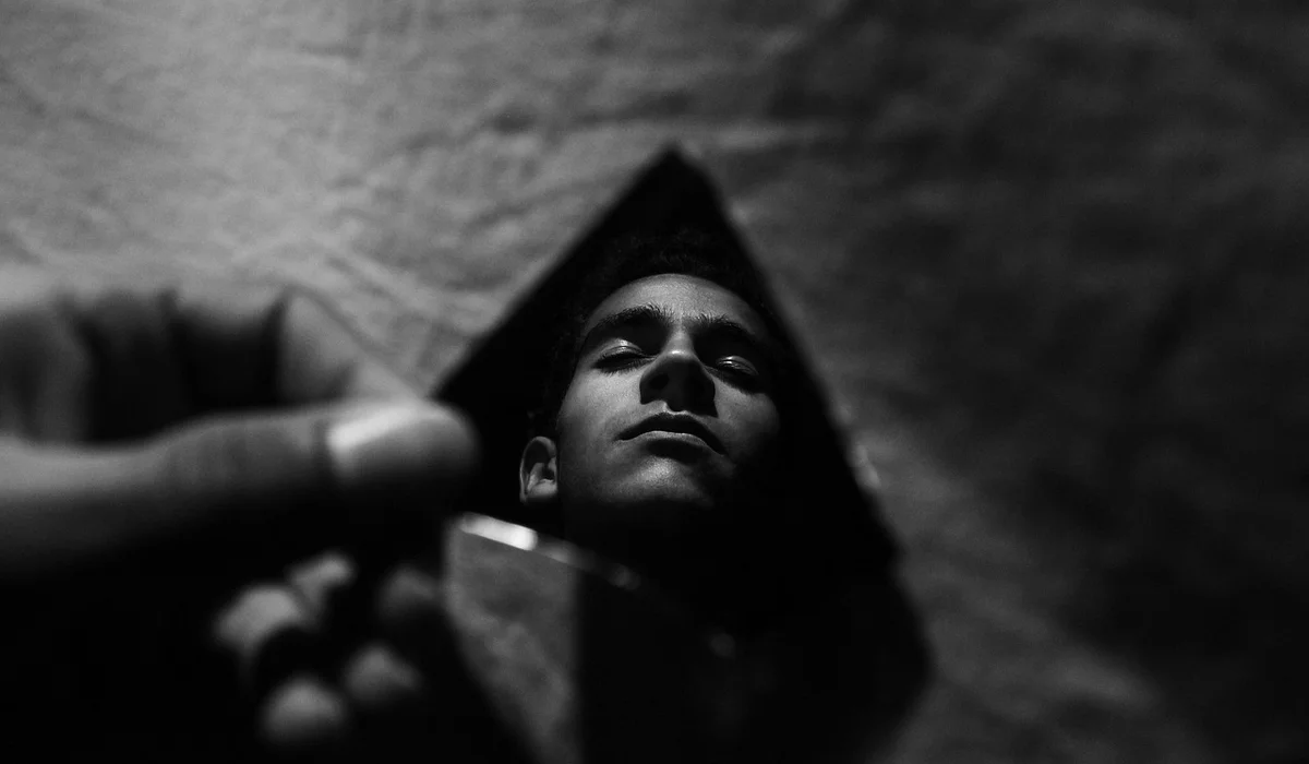 Black-and-white image of a child looking upward with a somber expression, while a hand reaches in from the left foreground.