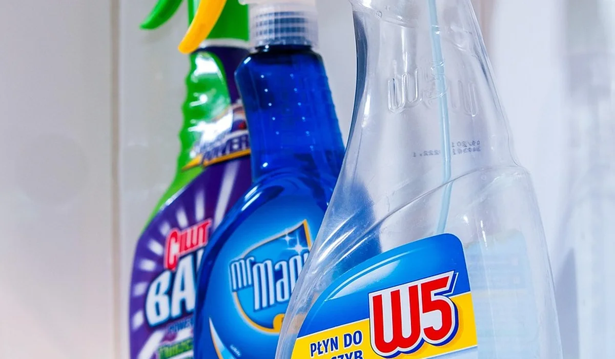 Assorted household cleaning spray bottles on a shelf, highlighting the toxic cleaners that can harm pet parrots.
