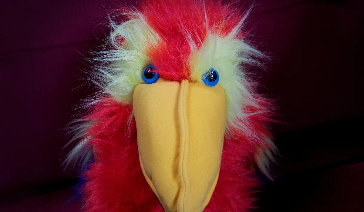 Close-up of a colorful plush parrot toy with a bright yellow beak, red and yellow feathers, and blue eyes.