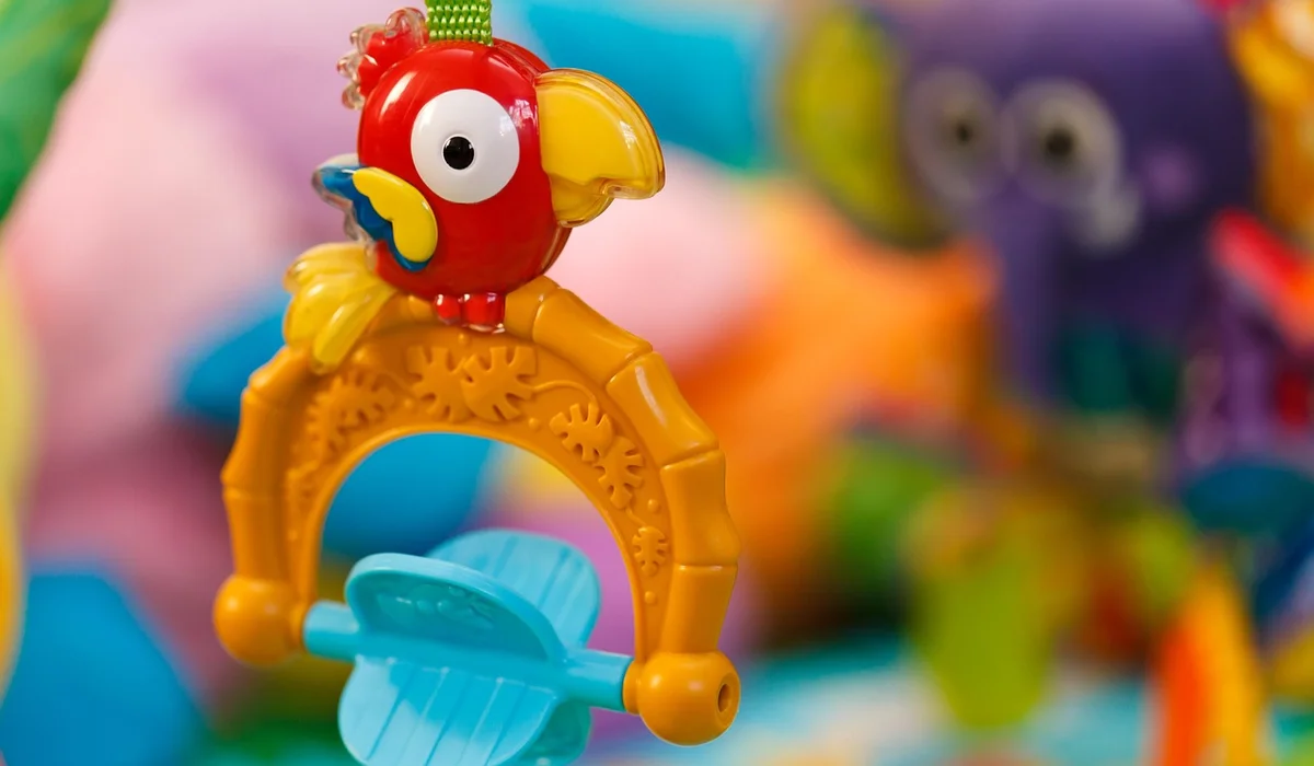 Close-up of a bright, colorful parrot toy with a red parrot figure perched on a yellow ring and blue paddles.