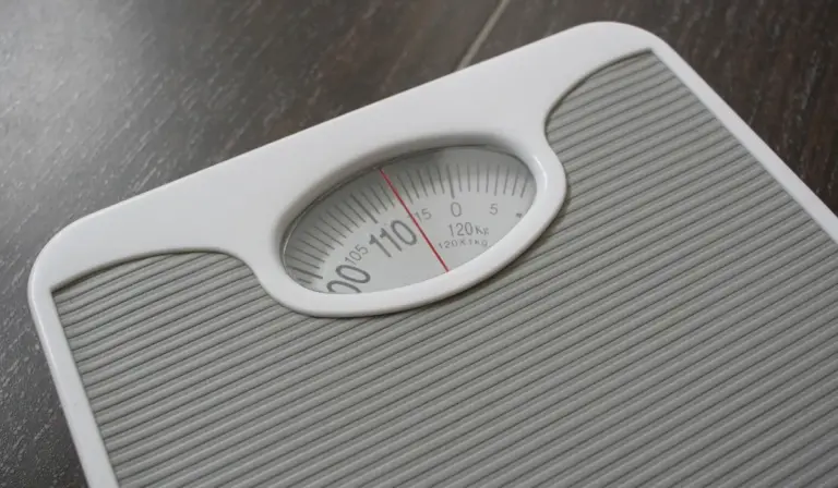 Close-up of a mechanical bathroom scale with a circular weighing dial.