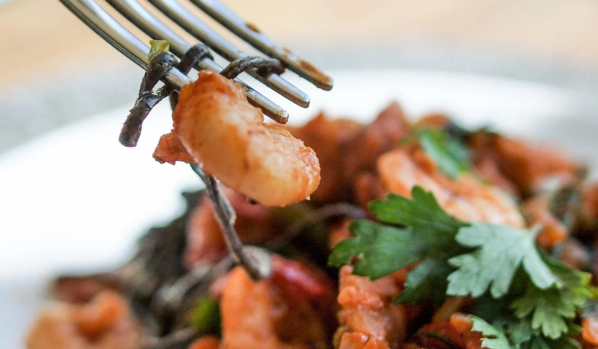 Close-up of a fork lifting a bite of pasta with herbs from a plated dish.