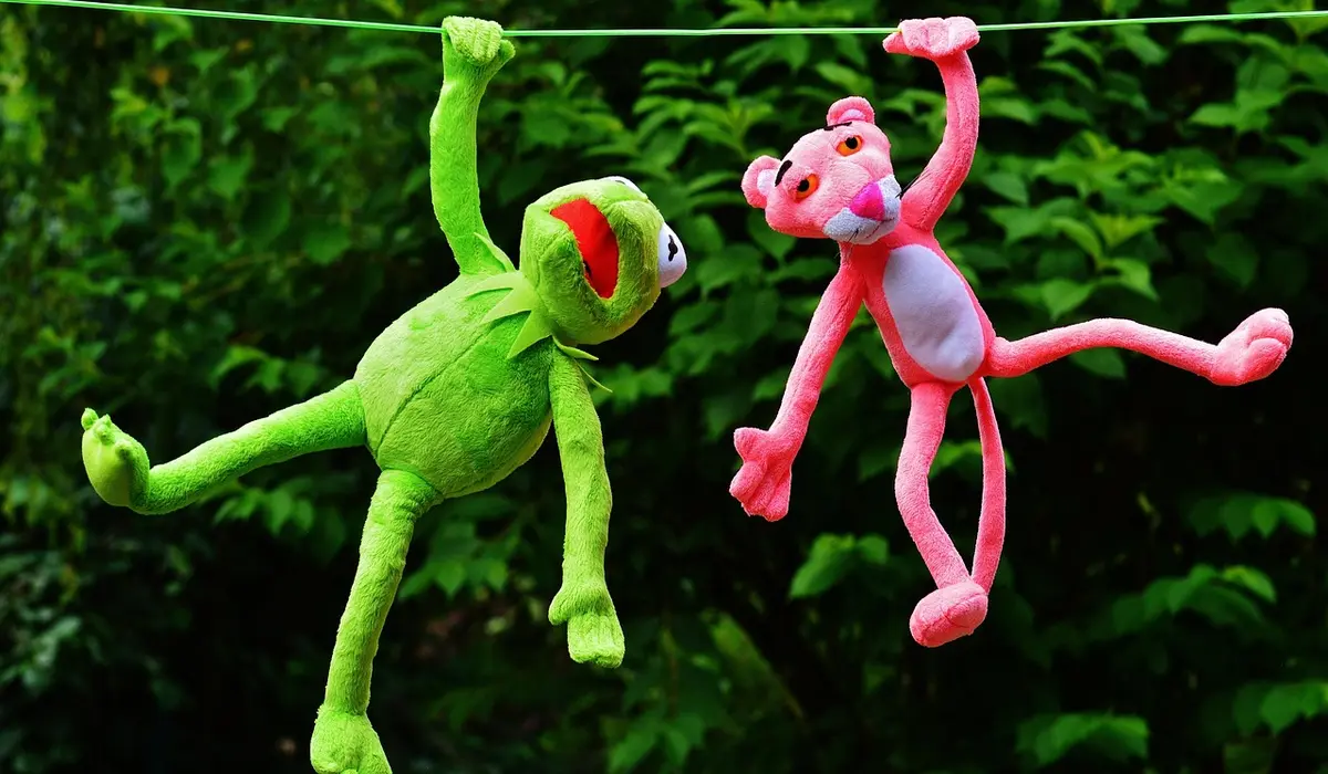 Two plush parrot toys hanging on a clothesline outdoors with green foliage in the background.