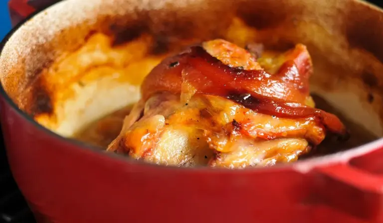 Red enameled pot containing a bubbling cheesy baked dish with browned edges