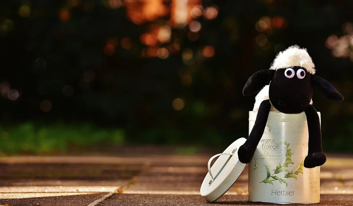 A plush black-and-white sheep toy sits on a metal can outdoors on a wooden deck, illustrating a simple homemade enrichment idea.